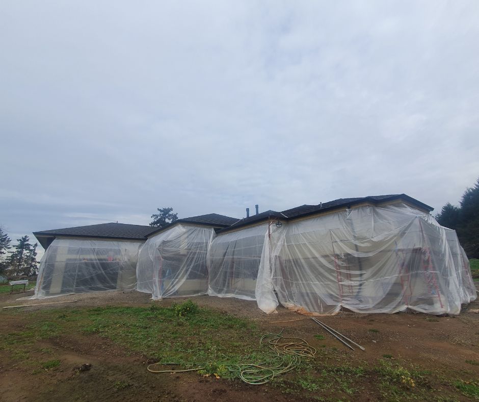 Installing a protective plastic bubble to repair stucco on a house during rainy weather in Oregon.