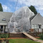 A large scaffolding bubble covered in plastic, protecting stucco repair work during heavy winter rains in Oregon