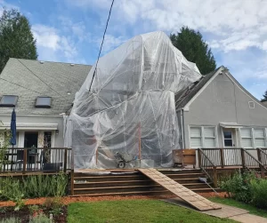 A large scaffolding bubble covered in plastic, protecting stucco repair work during heavy winter rains in Oregon